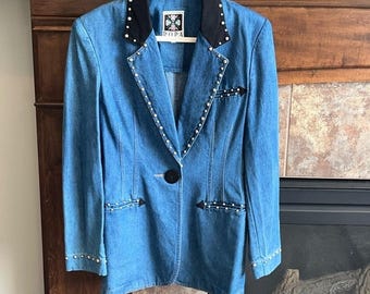 May include: A light blue denim blazer with a black collar and pearl accents. The blazer features a single black button closure and decorative arrow details. The collar has the text "DOPA".