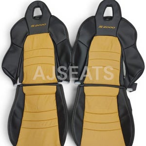 May include: Four car seat covers in black and tan. The seats have the text "S2000" in gold. The central panels are tan with horizontal stitching. The text "AJSEATS" is visible on the seats.