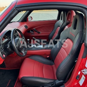 May include: Interior of a red sports car featuring black and red leather seats. The seats are embroidered with the word "S2000". The steering wheel and dashboard are black, contrasting with the red interior.