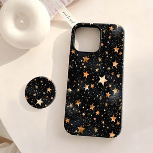 May include: Black phone case and matching pop socket with a gold star pattern. The case is designed to fit a smartphone and has a camera cutout. The pop socket is round and has a similar star design. The items are on a white surface.