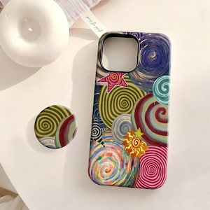 May include: A rectangular phone case and a matching circular phone grip featuring a vibrant, multi-colored pattern of painted swirls, spirals, and star shapes in shades of blue, green, pink, red, and yellow, with a black camera cutout.