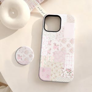 May include: A phone case and matching pop socket with a patchwork design featuring floral and gingham patterns in shades of pink and white. The phone case has a black camera cutout.