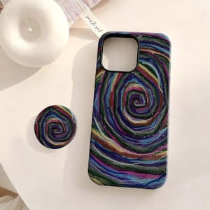 May include: A phone case and matching pop socket with a colourful, swirled design. The case is dark with a spiral of blues, greens, reds, and yellows. The pop socket has the same design. The case has a camera cutout.