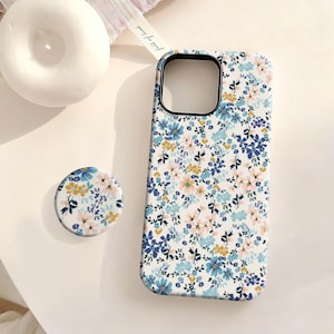 May include: White phone case and matching pop socket with a floral pattern in blue, yellow, and pink. The case has a black border around the camera cutout. The pop socket is round and has the same floral design.