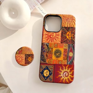 Può includere: Una custodia per telefono e un pop socket abbinato con un design patchwork con grafiche solari e celesti nei toni dell'arancione, rosso e giallo. La custodia ha un bordo nero attorno al ritaglio della fotocamera.