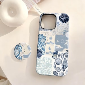 Pode incluir: Uma capa de telefone azul e branca com um pop socket a condizer. A capa apresenta uma colagem de ilustrações de conchas, cenas tropicais e o texto "GO WHERE YOU FEEL MOST ALIVE". O pop socket tem um design semelhante.