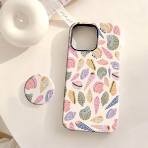 May include: A white phone case and matching pop socket featuring a colorful seashell pattern in shades of pink, blue, yellow, and green. The case has a black camera cutout.