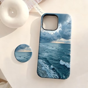 Może przedstawiać: Prostokątne etui na telefon oraz okrągły uchwyt do telefonu z pasującym motywem oceanu, przedstawiającym ciemnoniebieskie fale, białą morską pianę oraz zachmurzone niebo z kilkoma ptakami latającymi nad horyzontem.