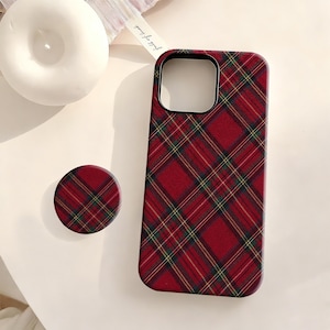 May include: A red tartan phone case and matching phone grip. The case is designed for a smartphone and features a repeating pattern of red, green, and yellow lines. The phone grip is round and has the same tartan design.