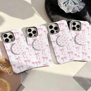 May include: Four white phone cases with a pink bow pattern and matching pop sockets. The cases have a repeating design of pink bows and small dots. The pop sockets also feature a bow pattern. The cases are for a smartphone.