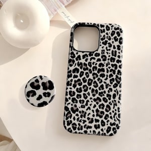 Könnte beinhalten: Ein Handycase und ein passender Pop-Socket mit einem schwarz-weißen Leopardenmuster. Das Case hat einen schwarzen Rand und eine Kameraaussparung. Der runde Pop-Socket hat das gleiche Leopardenmuster. Die Artikel liegen auf einer weißen Oberfläche.