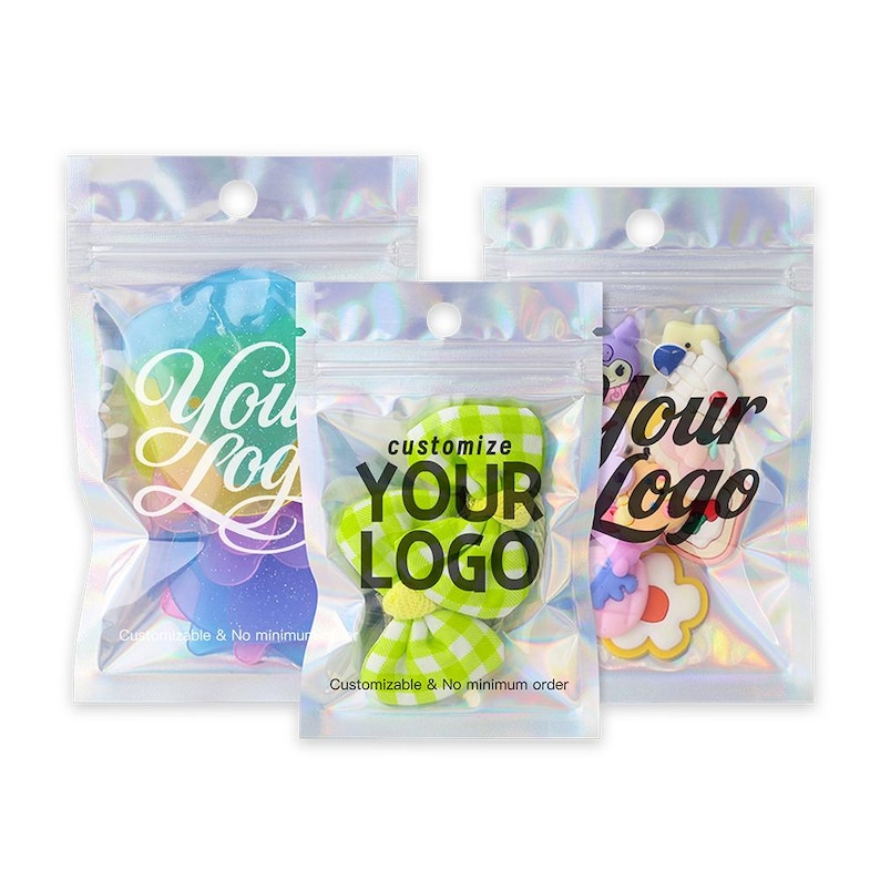 May include: Three clear, iridescent plastic bags with zipper closures. Each bag contains a colorful, custom-shaped item. Text on the bags reads "Your Logo" and "Customize Your Logo". The bags are sealed and ready for use.