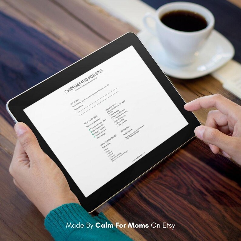 May include: A black tablet displaying a document titled "OVERSTIMULATED MOM RESET" with bullet points. The tablet is held by a person, with a cup of coffee in the background. The text "Made By Calm For Moms On Etsy" is at the bottom.
