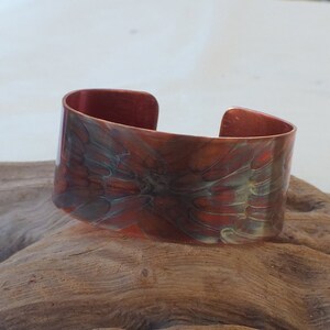 May include: A copper cuff bracelet with a hammered finish and a swirling pattern of red, orange, and green.