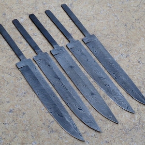 Könnte beinhalten: Fünf unfertige Stahlmesser mit gemusterter Oberfläche. Die Klingen sind diagonal angeordnet und zeigen ihre Form und ihr Design. Die Klingen haben ein dunkles, metallisches Aussehen, was auf eine robuste Konstruktion hindeutet.