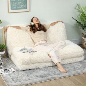 Könnte beinhalten: Ein flauschiges, cremefarbenes, modulares Sofa mit weicher, zotteliger Textur. Das Sofa befindet sich in einer entspannten Umgebung, die Komfort und Freizeit suggeriert. Das Design ist modern und einladend.