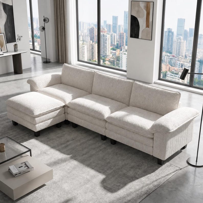 Pu&ograve; includere: Un grande divano componibile color bianco sporco con finitura in tessuto testurizzato, cuscini di seduta profondi e un pouf abbinato. Il divano presenta ampi braccioli arrotondati ed &egrave; sostenuto da piedini bassi di colore scuro.
