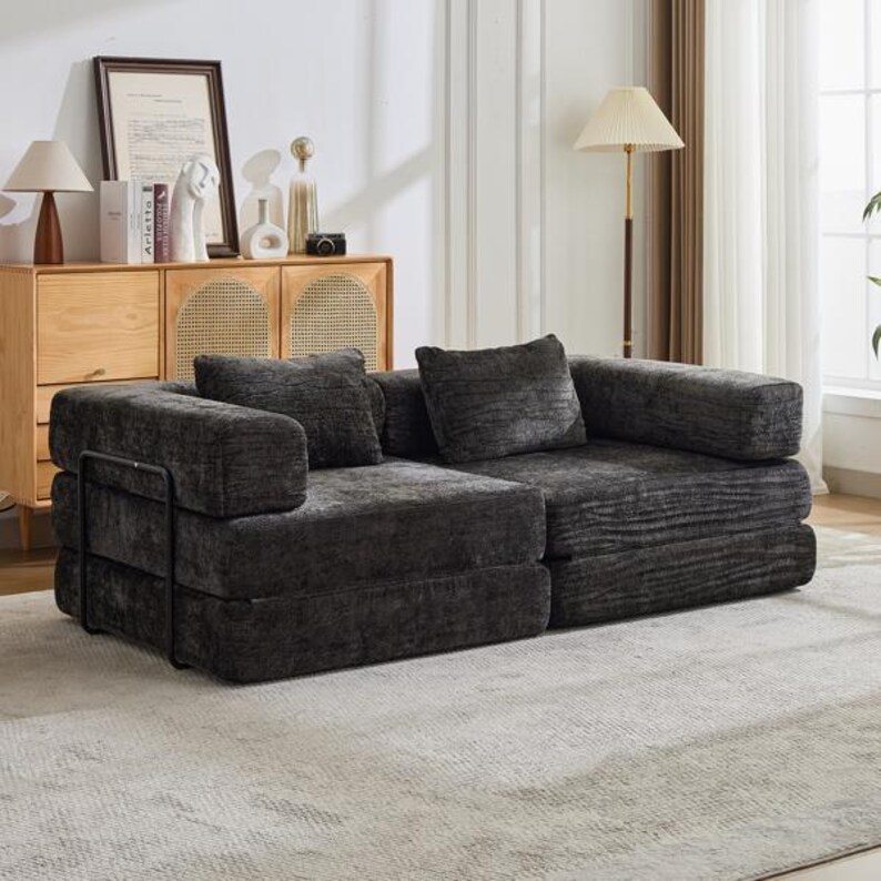 May include: A low-profile, modular sofa upholstered in dark charcoal grey textured fabric. The piece features two wide seat sections, two matching back cushions, and a thin black metal frame structure visible on the side of the armrest.