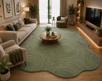 May include: A large, sage green area rug with an irregular, organic shape and a textured surface featuring concentric circular patterns. The rug covers a significant portion of the floor, providing a soft, plush foundation for the living room furniture.