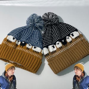 May include: Two knit beanies with pom-poms, one in blue and one in black, both featuring a repeating sheep pattern above a solid mustard-yellow ribbed cuff. The hats are displayed side-by-side, showcasing the detailed wool-like texture.