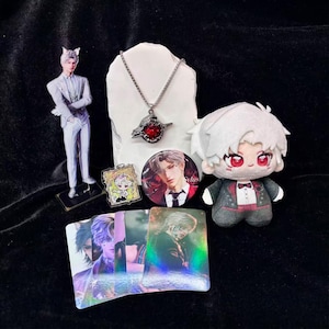 May include: A collection of anime-themed merchandise, including a figurine, plush doll, necklace, button, trading cards, and a small acrylic charm. The items feature a character with white hair and red eyes, and are arranged on a black surface.