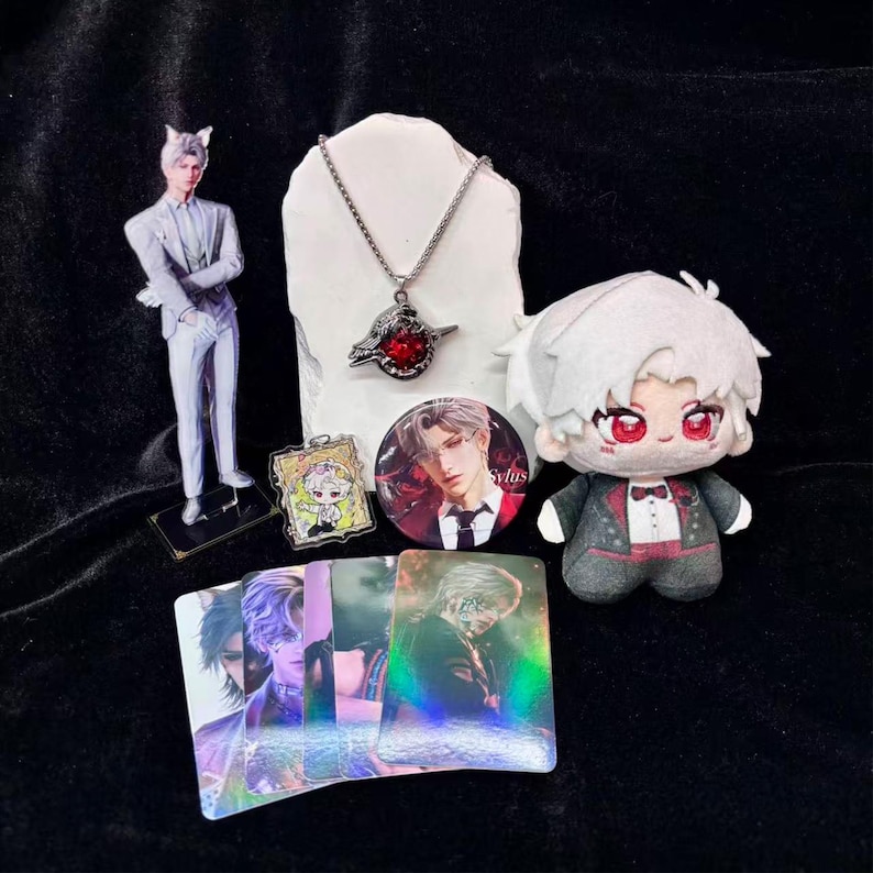 May include: A collection of anime-themed merchandise, including a figurine, plush doll, necklace, button, trading cards, and a small acrylic charm. The items feature a character with white hair and red eyes, and are arranged on a black surface.