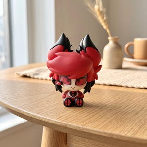 Puede incluir: Una peque&ntilde;a figura de vinilo estilizada que representa a un personaje con cabello rojo vibrante, mechones negros en forma de orejas y grandes ojos rojos. La figura tiene un rostro p&aacute;lido, una sonrisa sencilla y viste un traje rojo y negro.