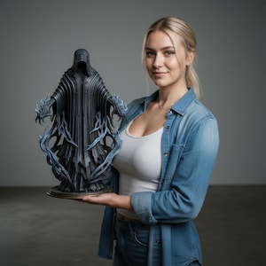 Może przedstawiać: Ciemnoszara statua postaci w kapturze z powiewającymi szatami i niebieskimi akcentami przypominającymi płomienie. Statua jest trzymana przez osobę ubraną w dżinsową koszulę i biały podkoszulek. Statua ma szczegółowy design.