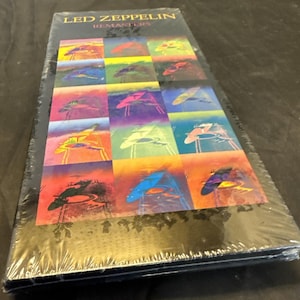 May include: A sealed CD case featuring the text "LED ZEPPELIN REMASTERS." The cover art displays a grid of colorful, abstract images. The case is wrapped in clear plastic, suggesting a new or unopened product.