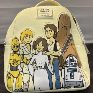 May include: A light yellow Star Wars Loungefly mini backpack featuring cartoon illustrations of Luke Skywalker, Princess Leia, Han Solo, Chewbacca, C-3PO, and R2-D2. The backpack has a top handle, a zipper closure, and a small rectangular tag that says "STAR WARS."