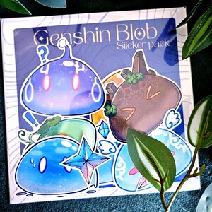 Peut inclure: Un paquet d'autocollants avec des personnages de blobs de dessins animés bleus, bruns et verts. Le texte "Genshin Blob Sticker pack" est visible sur l'emballage. Les autocollants ont un style de dessin animé avec des contours blancs.