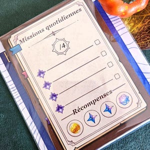 Op de afbeelding: Een beige kaart met de Franse teksten "Missions quotidiennes" en "Récompenses". De kaart heeft selectievakjes, ster- en muntillustraties en het nummer "1/4". De kaart zit in een doorzichtige plastic hoes.