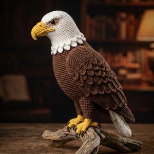 May include: A crochet eagle sculpture, featuring a white head, yellow beak, and brown body with detailed wing patterns. The eagle is perched on a wooden branch, displaying yellow talons. This decorative item is a handcrafted piece.
