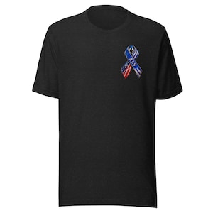 May include: A charcoal grey short-sleeve t-shirt featuring a small graphic on the upper left chest. The graphic is a ribbon design with a blue, white, and red American flag pattern, a silhouette of a person, and the text ALS printed in white.