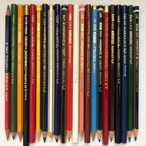 May include: A collection of colorful pencils, including red, blue, yellow, and green, arranged in a row. The pencils have various brand names and model numbers printed on them, such as "A.W. Faber-Castell" and "Goldfaber". The pencils are sharpened and ready for use.