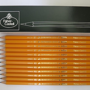 May include: A set of twelve yellow Faber-Castell Bonanza 1329 pencils arranged horizontally below a black rectangular box. The box features the white Faber-Castell logo and a line drawing of a pencil. Each pencil is marked with the brand name.
