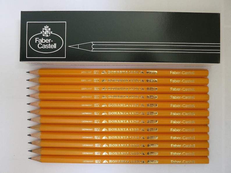 May include: A set of twelve yellow Faber-Castell Bonanza 1329 pencils arranged horizontally below a black rectangular box. The box features the white Faber-Castell logo and a line drawing of a pencil. Each pencil is marked with the brand name.