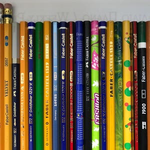 May include: A collection of pencils of various colors and designs, including red, yellow, green, and blue. The pencils are from the Faber-Castell brand and feature text such as "American Checking 1007" and "Fashion". The pencils have erasers.