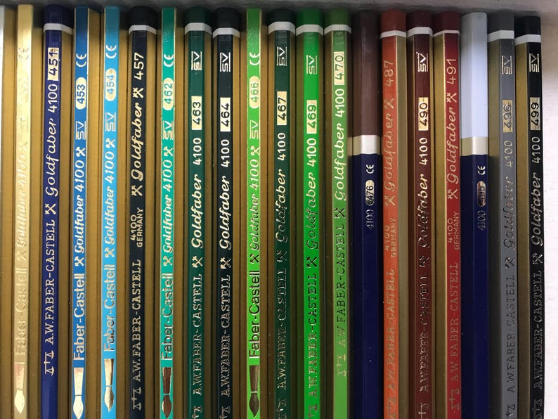 K&ouml;nnte beinhalten: Eine Sammlung von Goldfaber 4100 Bleistiften von Faber-Castell, vertikal angeordnet. Die Bleistifte sind in verschiedenen Farben erh&auml;ltlich, darunter Blau, Gr&uuml;n, Braun und Gold. Jeder Bleistift hat eine Nummer und das Faber-Castell-Logo.
