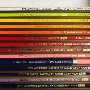 K&ouml;nnte beinhalten: Nahaufnahme einer Sammlung von Faber-Castell Goldfaber Bleistiften in verschiedenen Farben. Die Stifte sind horizontal angeordnet und zeigen ihre unterschiedlichen Farbt&ouml;ne sowie die Aufschriften "Goldfaber" und "4100". Die Stifte sind etwa 18 cm lang.
