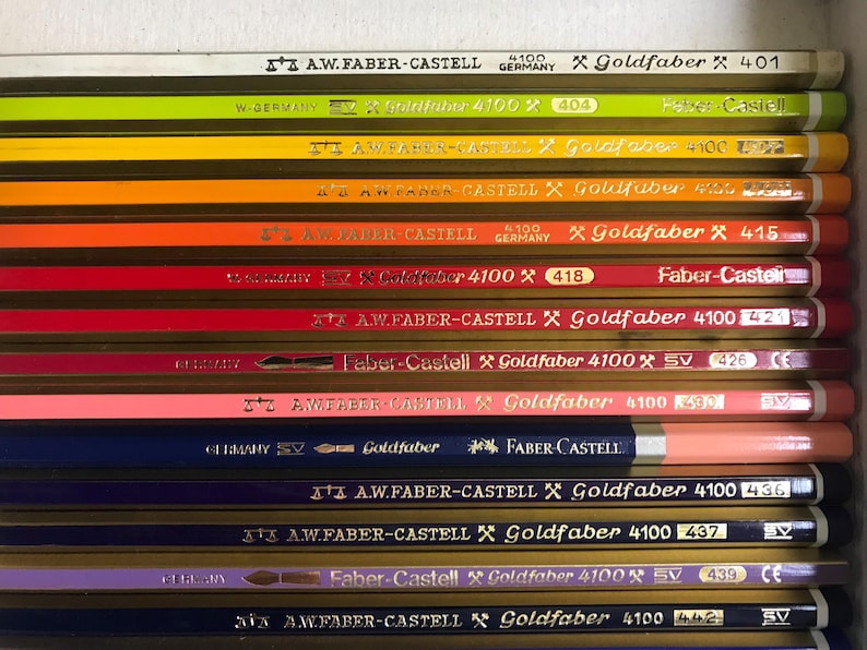 K&ouml;nnte beinhalten: Nahaufnahme einer Sammlung von Faber-Castell Goldfaber Bleistiften in verschiedenen Farben. Die Stifte sind horizontal angeordnet und zeigen ihre unterschiedlichen Farbt&ouml;ne sowie die Aufschriften "Goldfaber" und "4100". Die Stifte sind etwa 18 cm lang.