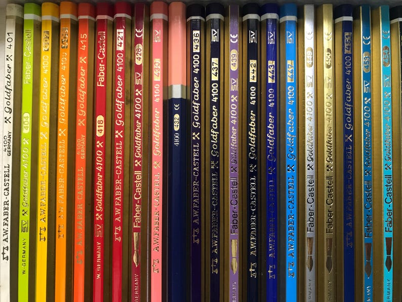 K&ouml;nnte beinhalten: Eine Sammlung von Faber-Castell Goldfaber 4100 Bleistiften in verschiedenen Farben, darunter Gelb, Orange, Rot, Rosa, Blau und Gold. Jeder Bleistift tr&auml;gt den Markennamen und die Modellnummer.