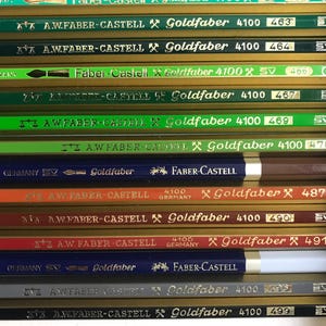 K&ouml;nnte beinhalten: Nahaufnahme einer Sammlung von Faber-Castell Goldfaber Bleistiften. Die Bleistifte sind in verschiedenen Farben, darunter Gr&uuml;n, Blau, Orange und Braun. Jeder Bleistift ist mit dem Markennamen Goldfaber und einer Nummer beschriftet.