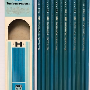 Puede incluir: Un juego de lápices Tombow Micro Crystallite turquesa, etiquetados 8414 H, junto a una caja a juego. La caja tiene el logotipo de Tombow Pencils y texto japonés. Los lápices son para uso escolar.
