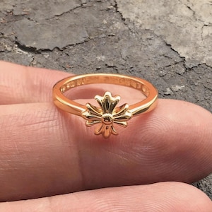 Può includere: Un anello in oro lucido caratterizzato da un motivo a croce centrale con bracci arrotondati a forma di petalo. La fascia è liscia e circolare, con una finitura metallica riflettente. Il design è simmetrico, con la croce integrata nell'anello.