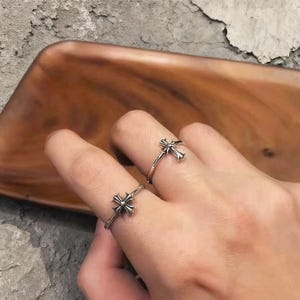May include: Two silver rings featuring a detailed cross emblem on the band. The rings have a polished metallic finish with darkened recessed areas to highlight the intricate cross design. Each ring is thin and circular, worn on separate fingers.