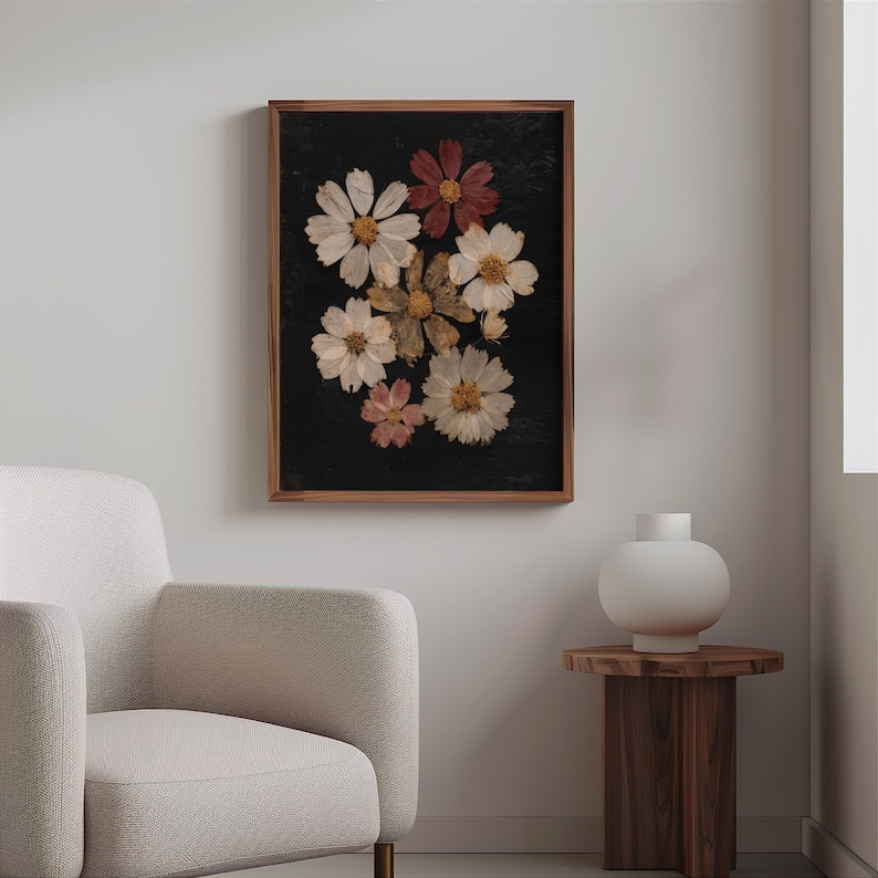 May include: A framed floral art print featuring a dark background with pressed flowers in shades of white, pink, and red. The flowers are arranged in a cluster, and the frame is made of wood. The artwork is displayed in a living room setting.