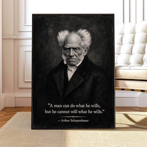 May include: A black and white portrait print of Arthur Schopenhauer in a dark coat, featuring the quote: "A man can do what he wills, but he cannot will what he wills." The artwork is framed in a thin black border and presented on a wall.
