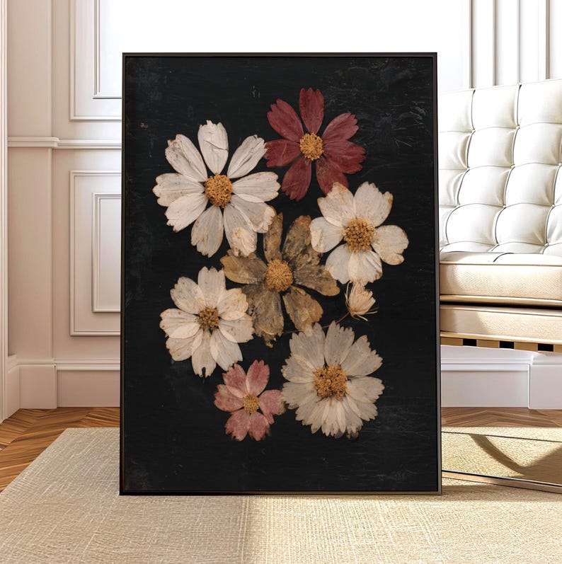 May include: A framed art print featuring a collection of pressed flowers against a black background. The flowers are in shades of white, pink, and brown, with yellow centers. The artwork is displayed in a black frame, suitable for home decor.