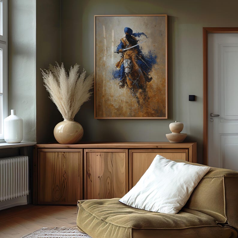 May include: A framed print shows a figure on horseback, in blue, brown, and gold tones. It hangs above a wooden cabinet, with a vase of dried pampas grass and a white cushion on a green sofa. The room has a neutral colour scheme.